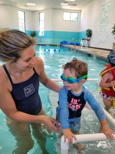A Saint Basil child with goggles being supported by a swim teacher in the pool participating in the aquatics program