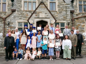 Graduates holding their diplomas along with other students and adults in front of the Saint Basil Academy's front door