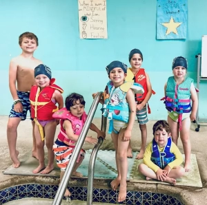 children in bathing suits standing on the edge of the swimming pool