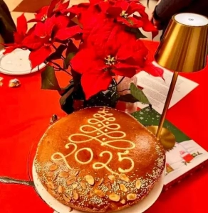 Vasilopita with 2025 on top sitting in front of a poinsettia on a red table cloth