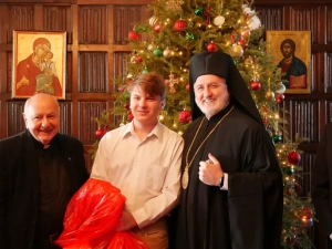 Archbishop Elpidophoros and Father Costa with a young man in front of a Christmas tree