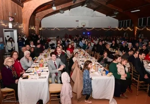 People sitting at rows of table with Christmas decorations hanging on the walls of a gymnasium