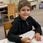 A Saint Basil Academy student smiling while holding a green crayon
