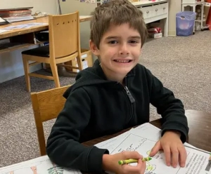 A Saint Basil Academy student smiling while holding a green crayon