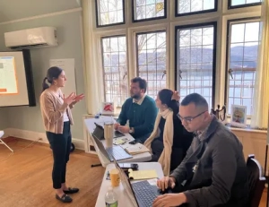 A lady speaking at a training at Saint Basil Academy with three people sitting at tables