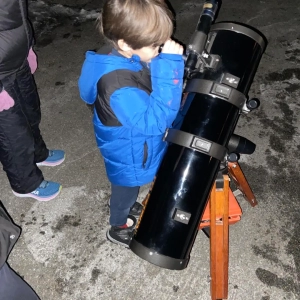 A boy looking into the eyepiece of a telescope at night