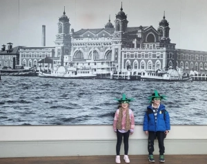 A girl and a boy standing in front of a mural of Ellis Island