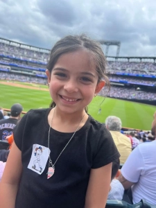 A girl smiling at a Mets game with the playing field behind her