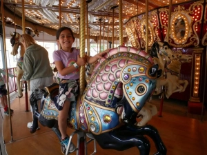 A girl riding a horse on a carousel at an amusement park.