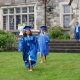 Two Saint Basil graduates dressed in cap and gown walking in the grass in front of Saint Basil Academy's main building.