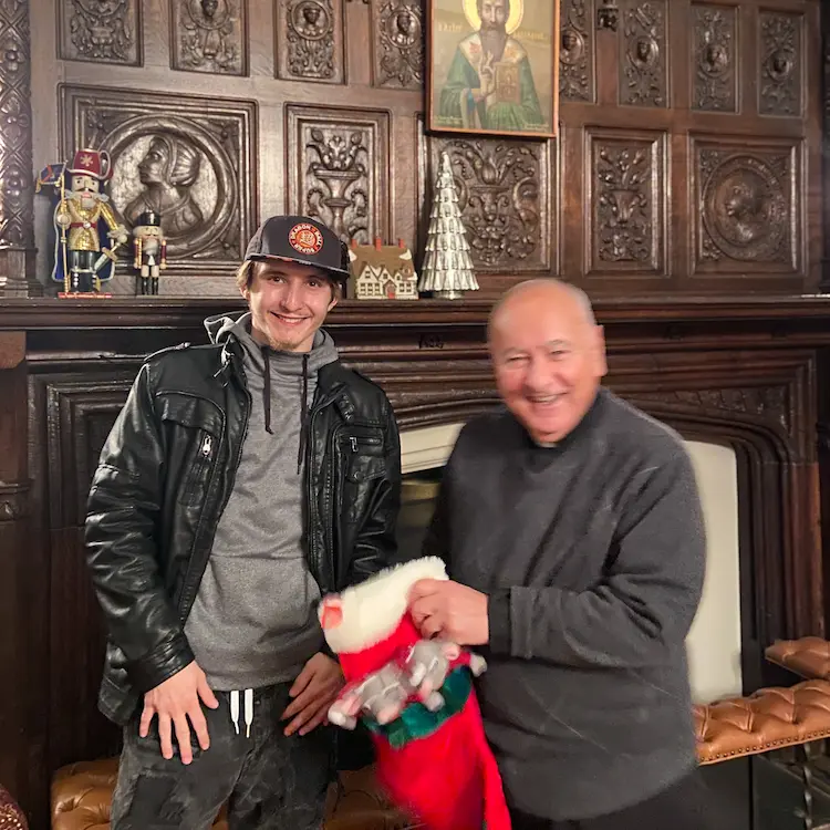 A male youth receiving a stocking from Father Costa in front of a fireplace