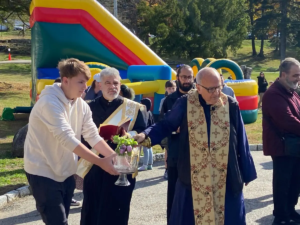 Father Costa dipping basil in water outside at Saint Basil Academy with others behind him