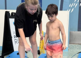 A young boy getting surfing instructions from a young lady before they get into the pool.