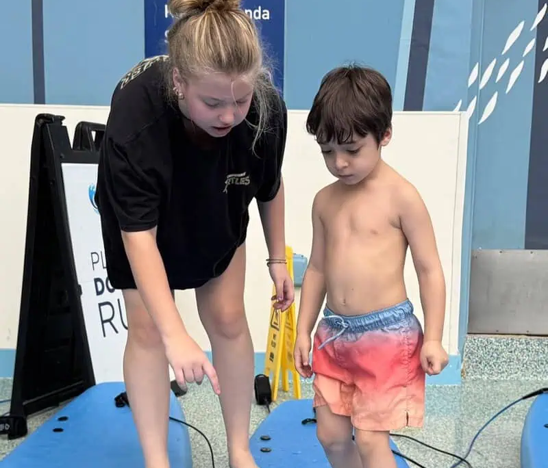 A young boy getting surfing instructions from a young lady before they get into the pool.