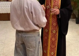 Father Nikolas Delaveris applying oil to the hand of a female youth
