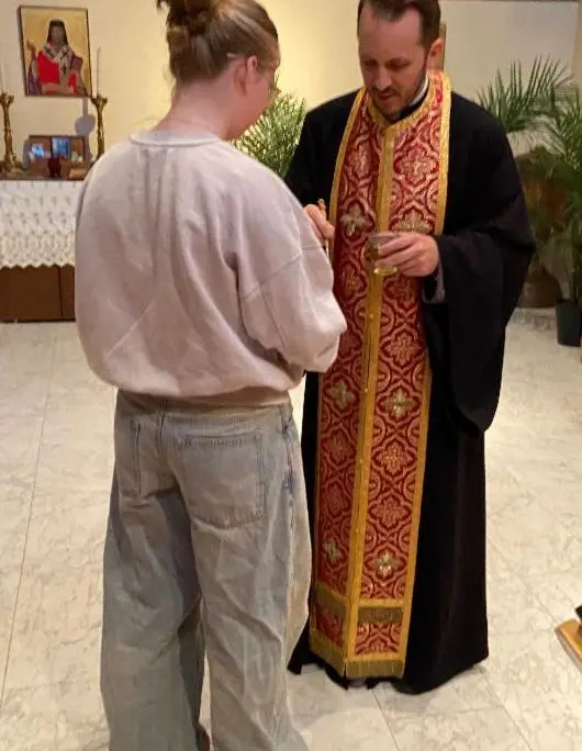Father Nikolas Delaveris applying oil to the hand of a female youth