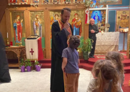 Father Nikolas Delaveris pointing to his nose while talking with a boy at the front of the Saint Basil chapel sanctuary