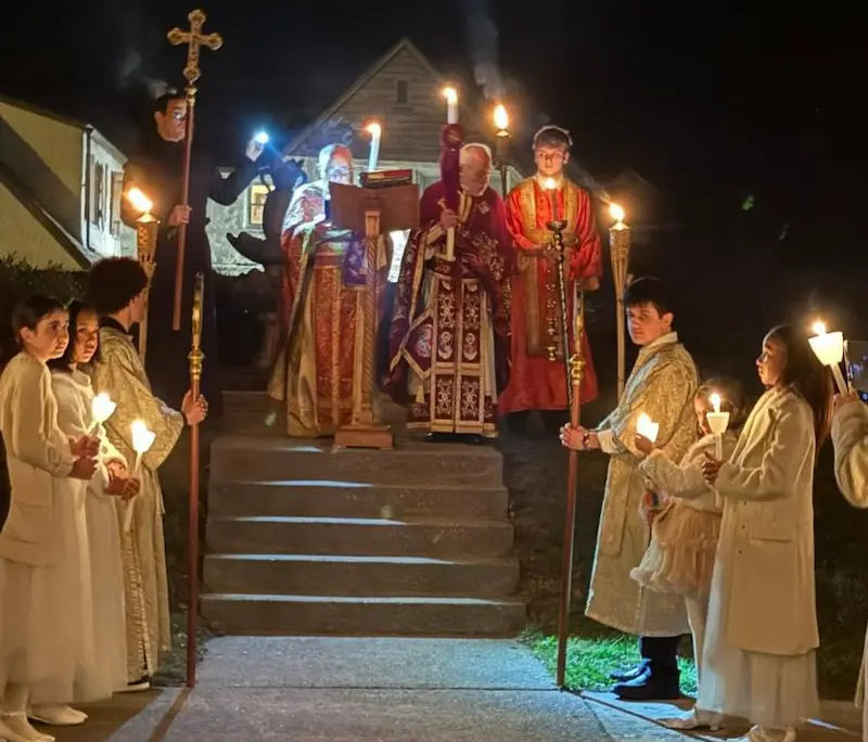 Two priests with the gospel and alter servers holding candles outside in the dark during the Holy Pascha service 2026