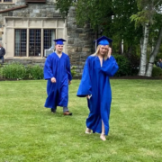 Two high school graduates in cap and gown walking across the lawn at Saint Basil Academy