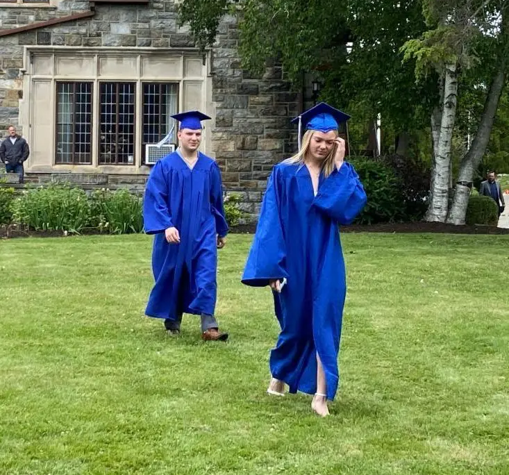 High school graduates Two high school graduates in cap and gown walking across the lawn at Saint Basil Academy