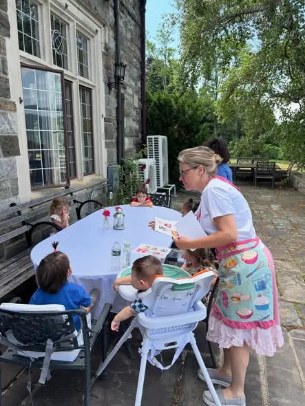 Restaurant day at the playroom A lady holding a menu standing at a table with children seated around it on restaurant day at the playroom.