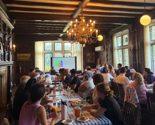 Saint Basil Academy staff sitting at two long adjacent tables with a projector screen at the far end of the room.
