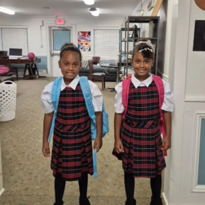Two girls smiling with their dresses and backpacks on, ready for a new school year