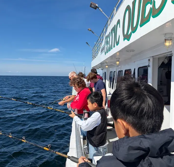 Fishing trip Two boys holding fishing poles over the railing of a boat with adults in the background