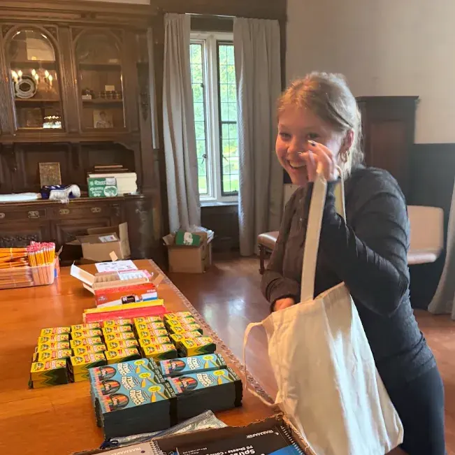 Making back-to-school kits A girl putting school supplies in a white canvas tote bag